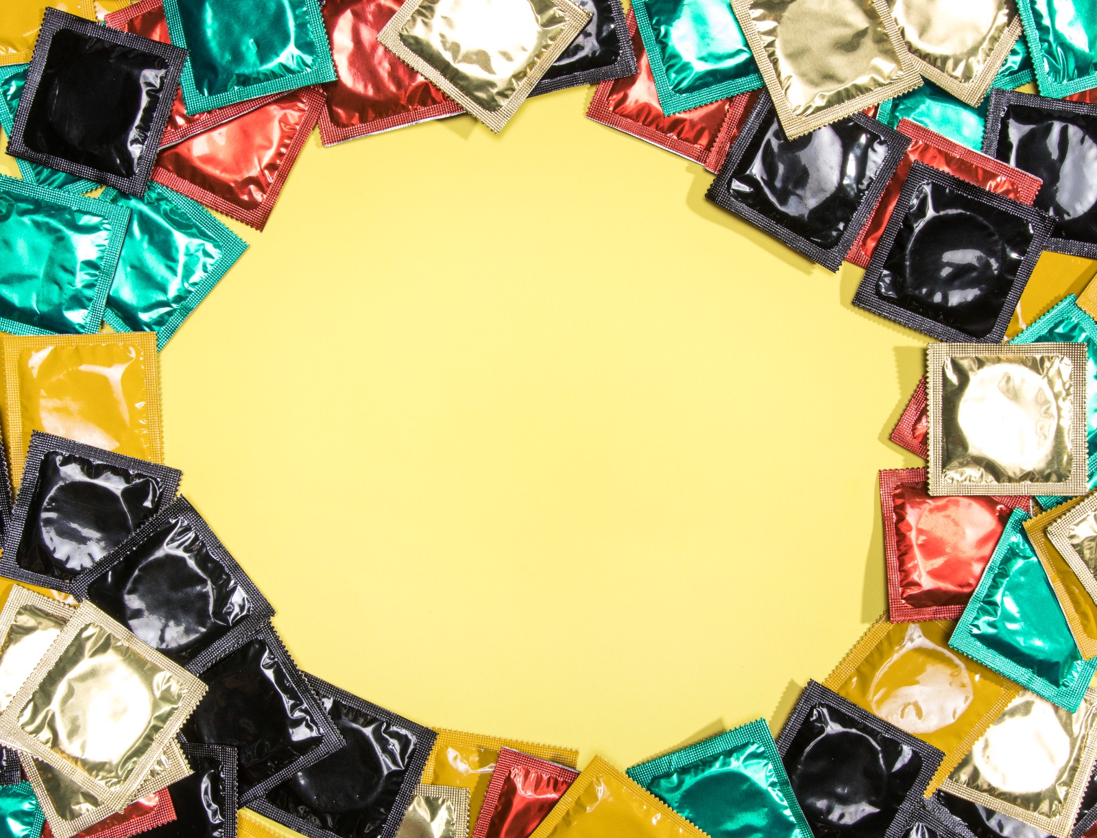 Diversos pacotes coloridos de preservativos dispostos em círculo sobre um fundo amarelo vibrante, com um espaço vazio redondo no centro para texto.